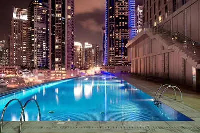 a large swimming pool in a city at night at Twisting Tower Stay a Chic 2BR in Cayan Tower in Dubai
