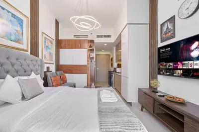 a bedroom with a large white bed and a kitchen at Bright & Cozy Studio in Vibrant Azizi Riviera in Dubai