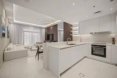 a kitchen with white cabinets and a living room at Brand New Luxury 2BHK Apartment in Jadeel 2 MJL in Dubai