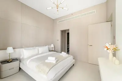 a white bedroom with a large bed and a table at VayK - Refined 1 BD Apartment in JVC in Dubai