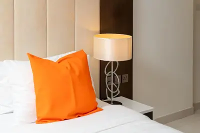 a bed with an orange pillow and a lamp at Full Burj Khalifa View New Year Fireworks - DAMAC Maison Distinction in Dubai