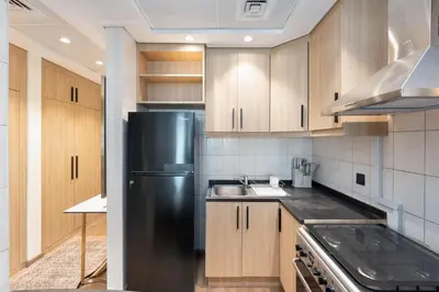 a kitchen with a black refrigerator and wooden cabinets at White Sage Discovery Gardens Renovated Studio next to Metro in Dubai