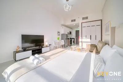 a white bedroom with a large bed and a tv at Elz Residence Stylish Studio Living in Dubai