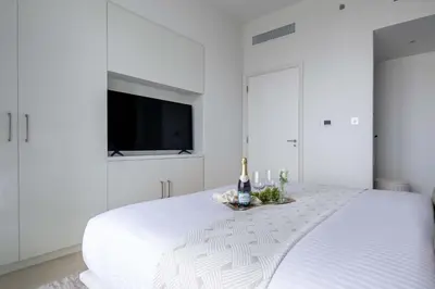 a white bedroom with a bed with a tv on the wall at Frank Porter - Downtown Views II Tower 1 in Dubai