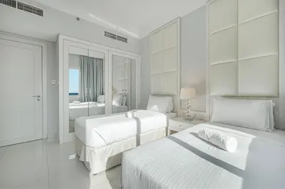 a white bedroom with two beds and a bathroom at Burj Khalifa view - 2 BR apartment in Downtown in Sabkhah