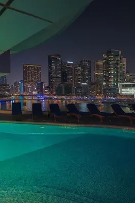 a pool with chairs and a city skyline at night at Rare apt with views of both Marina and JBR wheel in Dubai