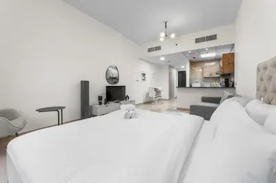 a white bedroom with a large bed and a living room at StayShort - Chic Studio Apartment in JVC Sleeps 4 in Dubai