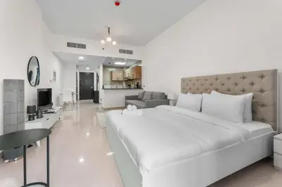 a white bedroom with a large bed and a living room at StayShort - Chic Studio Apartment in JVC Sleeps 4 in Dubai