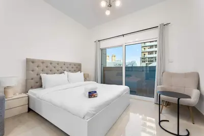 a white bedroom with a bed and a chair at StayShort - Chic Studio Apartment in JVC Sleeps 4 in Dubai