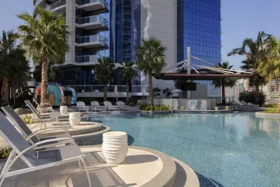 a swimming pool with chairs and palm trees in a city at EagleEye Paramount Tower D 1BR Sleeps 4 in Dubai