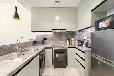 a kitchen with white cabinets and a stainless steel appliance at ALiving Elegant 1BR I Golf Gate, DAMAC Hills in Dubai