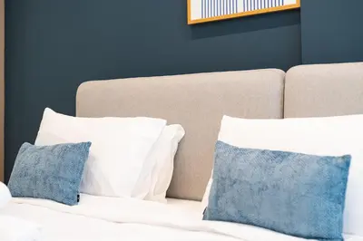 a bed with white pillows and a blue wall at HAVN - Modern Studio in Dusk, Al Barsha in Dubai