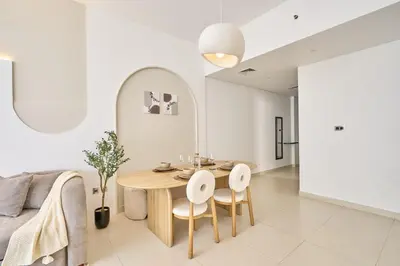 a white living room with a wooden table and chairs at Luxury 1BR Downtown Modern Urban Stay in Dubai