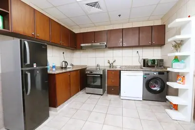 a kitchen with stainless steel appliances and wooden cabinets at Deluxe Ensuite Room with Balcony & Twin Beds in Dubai