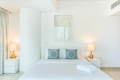 a white bedroom with a white bed and two lamps at RH- Marina Living- Chic Ocean Heights 3BR with Panoramic Views in Dubai