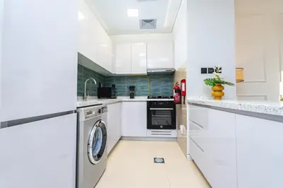 a kitchen with white cabinets and a washer and dryer at Escape24 Chic 1BR in Al Furjan near Metro in Dubai