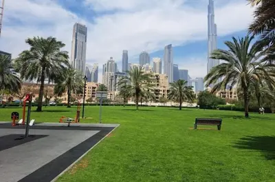 a park with a bench and palm trees in a city at Vogue Downtown Bellevue Towers near Burj Khalifa and Dubai Mall, One Bedroom Apartment with City View, Full Access to all Amenities in Dubai