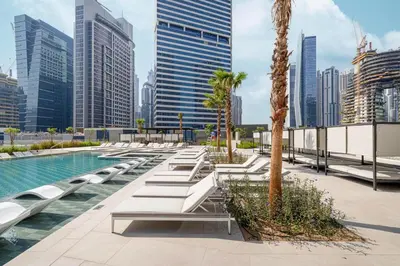 a pool with benches and palm trees in a city at StayMada - Peninsula Luxury Apartment with Balcony in Dubai