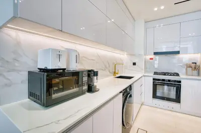 a white kitchen with a microwave on a counter at PVH - Binghatti Lavender - Tranquil Modern 1BR - Near JVC Community Park in Dubai