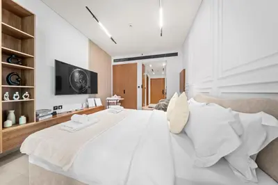 a white bedroom with a large bed and a tv at Brand New Luxury Studio, Amazing Pool & Gym in Dubai
