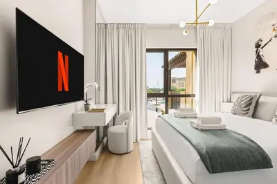 a white bedroom with a large bed and a tv at Modern and family friendly 1 bed in Dubai