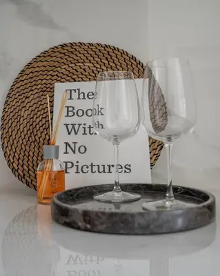 two wine glasses on a tray with a book with no pictures at GuestReady - Sunny Retreat near Dubai Frame in Dubai