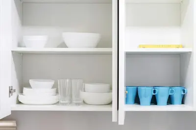 a white cabinet filled with bowls and plates and cups at New Large 2BR Apt Sleeps 10 Adults with Pool Gym Parking and Wifi in Dubai