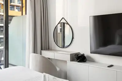 a white bedroom with a mirror and a tv at Chic Modern Studio in Meydan Azizi Riviera 26 in Dubai