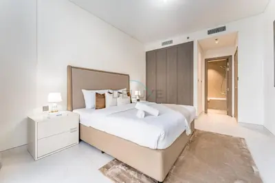 a white bedroom with a large bed and a bathroom at Glimpse of Burj Khalifa 2BR, 15-Minute Drive to Burj Khalifa and Downtown Landmarks, District One Phase III Residences 13, Mohammed Bin Rashid Al Maktoum City by Deluxe Holiday Homes in Dubai