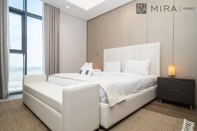 a white bed in a room with a large window at Mira Holiday Homes - High View 2 Bed Oasis at Nobles Tower with Sauna in Dubai