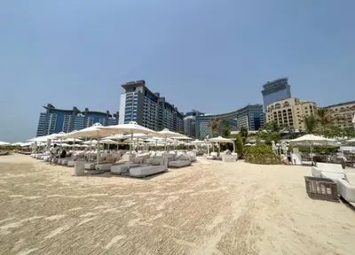a beach with white chairs and umbrellas and buildings at Séjour raffiné et inoubliable in Dubai
