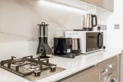 a white kitchen with a stove and a microwave at Azizi Riviera 5, Meydan Close to Downtown - Onelink in Dubai
