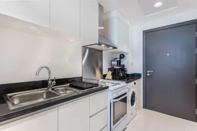 a white kitchen with a sink and a stove at Sky-High Luxury Studio Overlooking Trump Golf Club-Carson A, DAMAC Hills, Dubai in Dubai