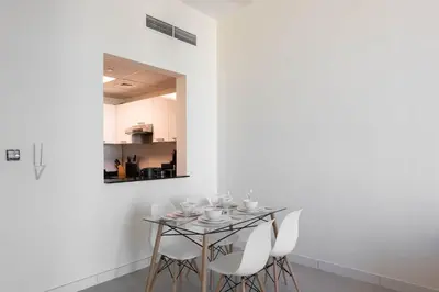a dining room with a glass table and white chairs at Bright & Modern 1BR La Rivera Apartments, JVC in Dubai