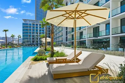 an umbrella and lounge chairs next to a swimming pool at Bright 1BR Apartment in Binghatti Phoenix High-Floor Views in Dubai