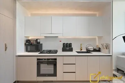 a kitchen with white cabinets and black appliances at Bright 1BR Apartment in Binghatti Phoenix High-Floor Views in Dubai