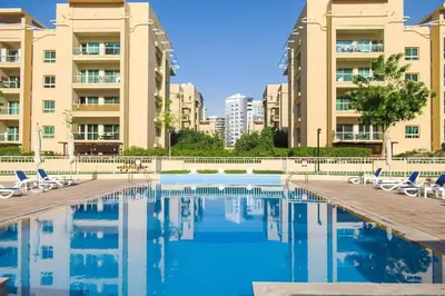 a swimming pool with chairs and some buildings at Upgraded Serene 1BR Retreat in The Greens in Dubai