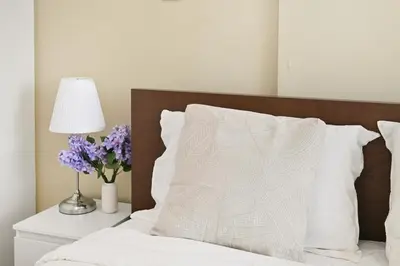 a bed with white sheets and a lamp and purple flowers at Dubai JVC - Oxford Residence 2 - Parking&Balcony in Dubai