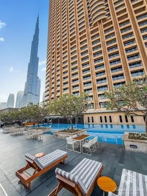 a pool with tables and chairs in front of tall buildings at Emaar Residences Fashion Avenue - 1BR - Connected to Dubai Mall - Pool with Burj View in Dubai