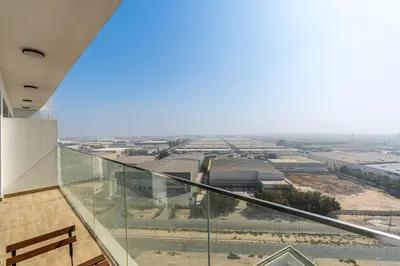 a glass balcony with a view of a factory at Cozy 1BR Apartment, 20 Min to Jebel Ali Beach in Dubai