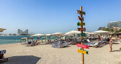 a beach with chairs and umbrellas and people at 1BR Apartment Anantara Palm Private Beach in Dubai