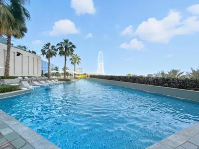 a swimming pool with chairs and palm trees at Brand New 1BD in Address JBR, Relaxing Stay for 2 in Dubai