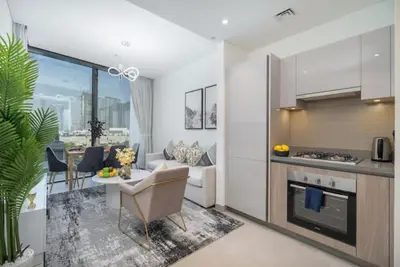 a kitchen and living room with a table and a couch at Vogue Al Maktoum City Sobha Hartland Waves Near to Downtown, Burj Khalifa and Dubai Mall, One Bedroom Apartment plus Kids room with Balcony and City View, Access to all Amenities in Dubai