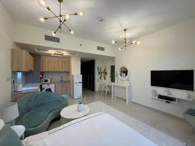 a living room with a green couch and a kitchen at Canal View Studio AG Tower in Dubai
