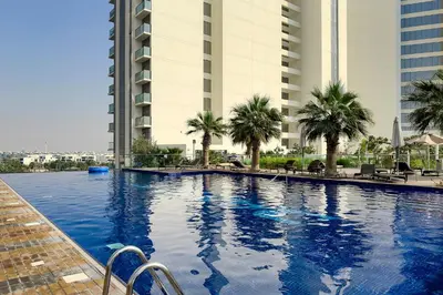 a large swimming pool with palm trees and buildings at Stylish 1BR Apartment at Damac Hills Golf Gate in Dubai