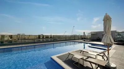 a large swimming pool with a umbrella and a table and chairs at Swanky Studio with Balcony in Dubai Hills Estate in Dubai