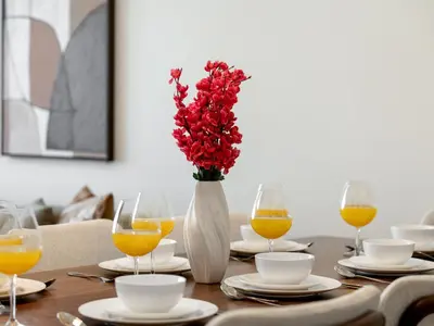 a table with a vase of red flowers and glasses of orange juice at Royal Vista - Luxe 4BR Penthouse with Burj Khalifa View at Imperial Avenue - Downtown in Dubai