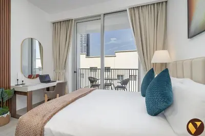 a bedroom with a bed and a desk with a laptop at Vogue JVC Luma22 near Circle Mall, Studio Apartment with Balcony and Vibrant Community View, Access to all Amenities in Dubai