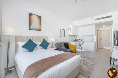 a bedroom with a large white bed and a kitchen at Vogue JVC Luma22 near Circle Mall, Studio Apartment with Balcony and Vibrant Community View, Access to all Amenities in Dubai