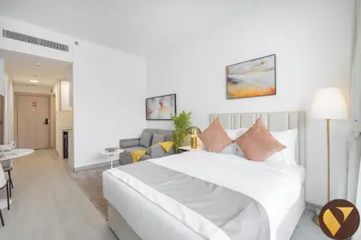 a white bedroom with a bed and a living room at Vogue JVC Luma22 near Circle Mall, Studio Apartment with Balcony and Vibrant Community View, Access to all Amenities in Dubai